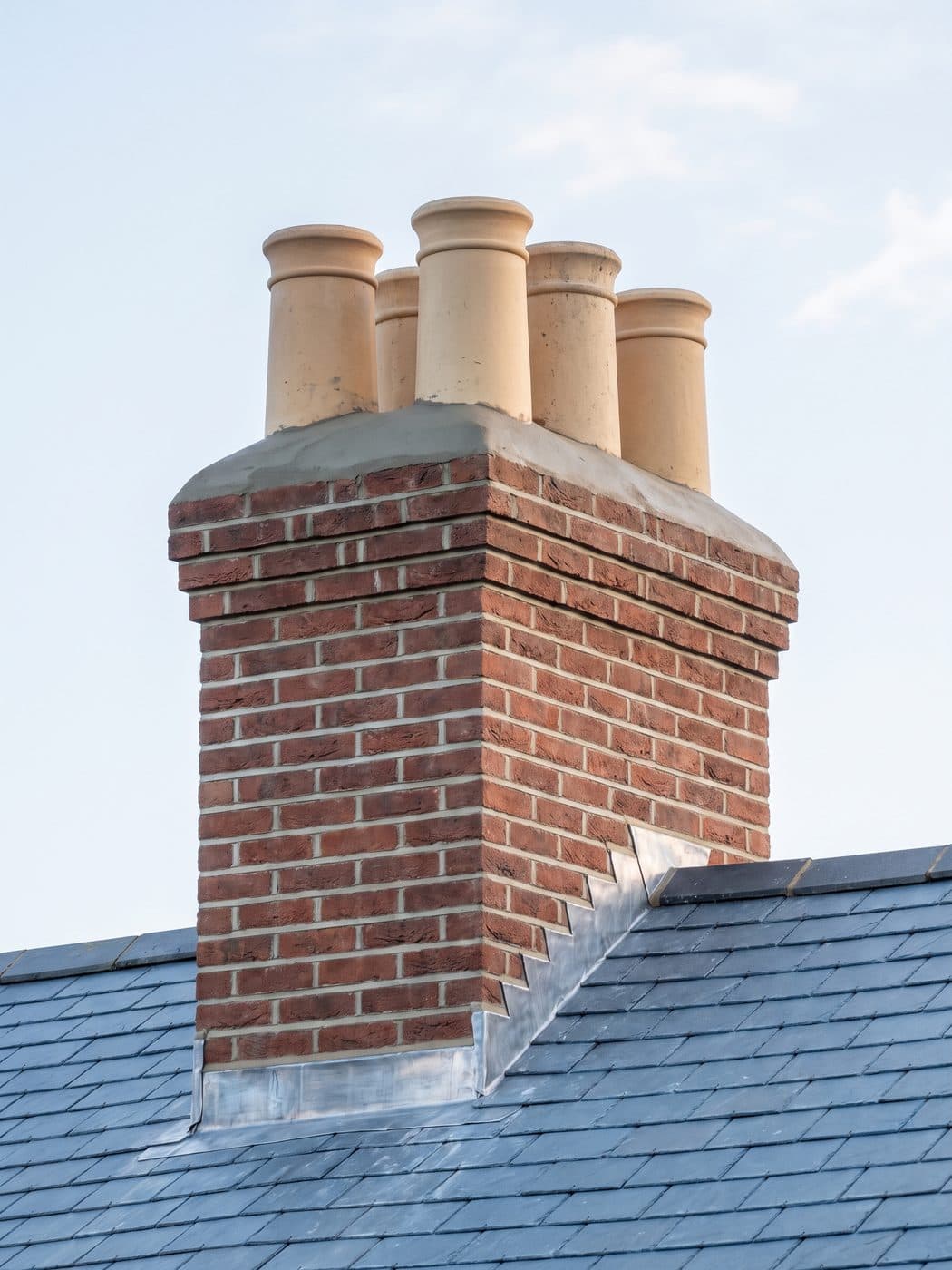 A rebuilt and repointed brick chimney stack with clean clay pots and new lead flashing
