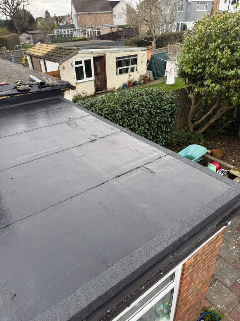 A finished dark flat roof on a single-storey extension, with edge trims and a garden beyond