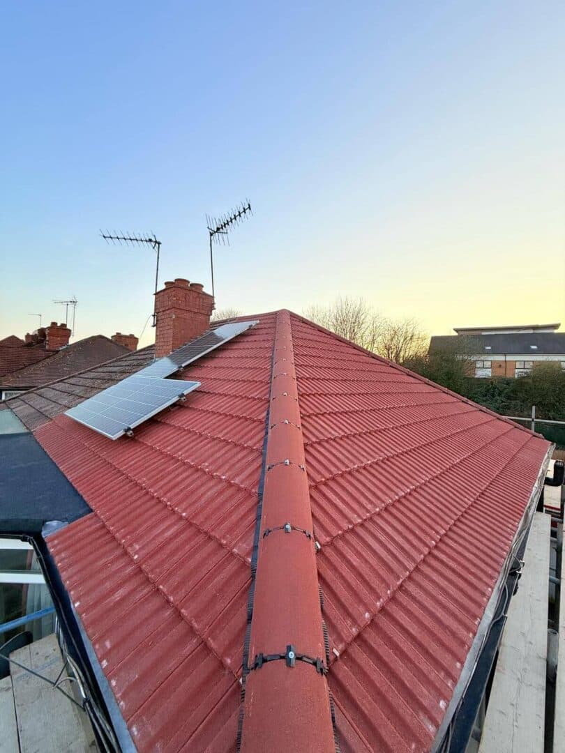 Looking along the ridge of a red tiled roof with solar panels on the slope and a brick chimney