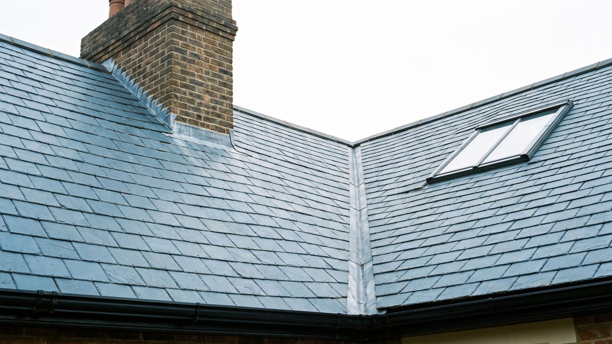 A house roof showing slate, a chimney with lead flashing, a valley, a rooflight and guttering together