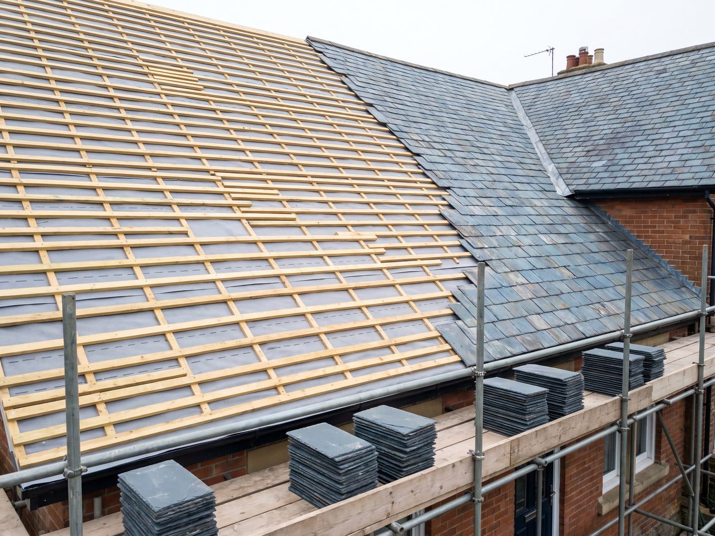 A roof stripped back to new battens over breathable membrane, with new slate stacked on the scaffold