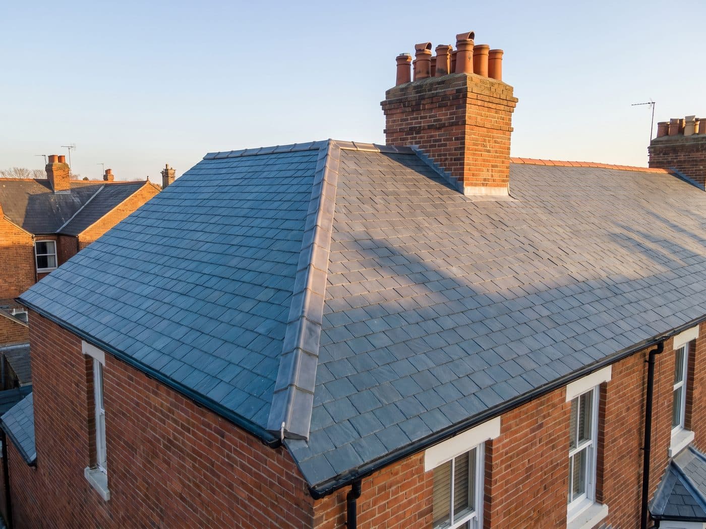 A completed natural slate roof on a Victorian terrace with even courses and a lead ridge