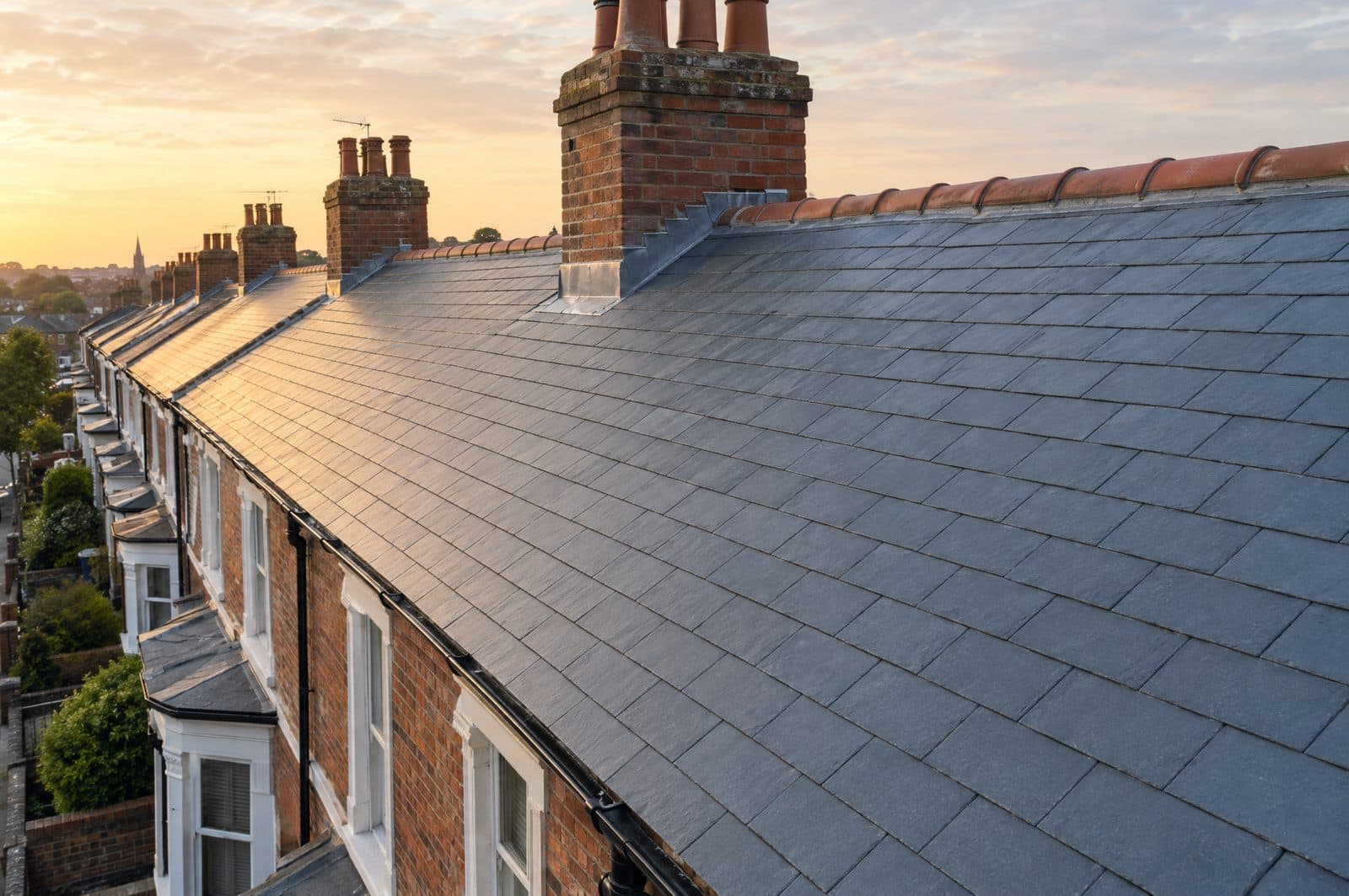 A completed natural slate roof on a Victorian terrace with straight courses, clay ridge tiles and a brick chimney